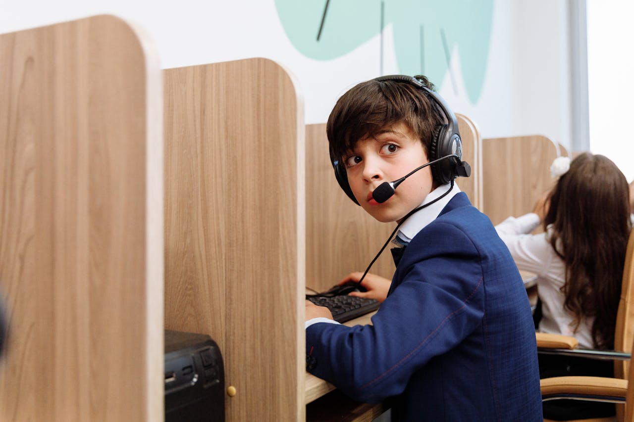 services-03 A boy in a blue suit wearing headphones focused in an educational setting with wooden cubicles.